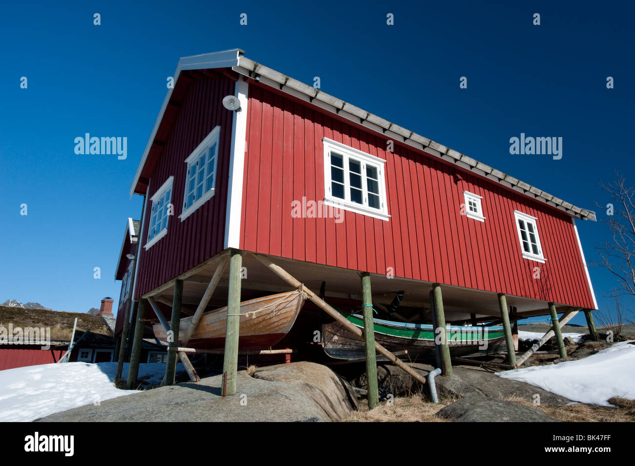 Traditional red wooden Rorbu fisherman`s hut with fishing boats stored below in village of Reine in Lofoten Islands in Norway Stock Photo